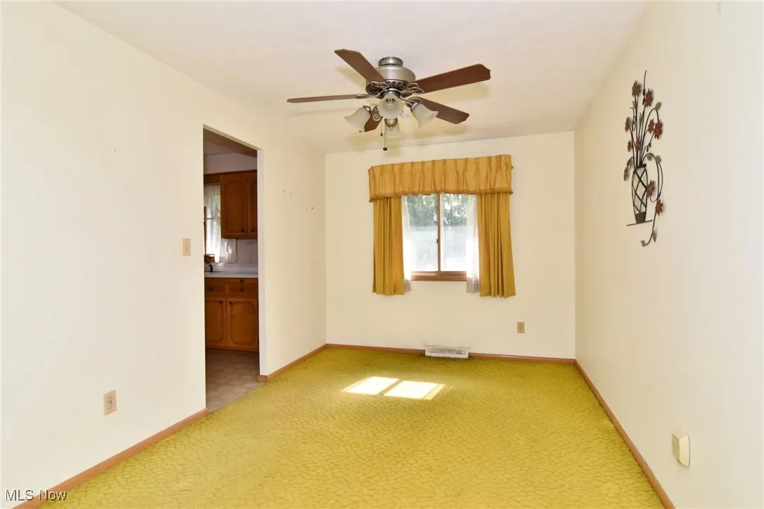 Empty room featuring light colored carpet, ceiling fan, and baseboards
