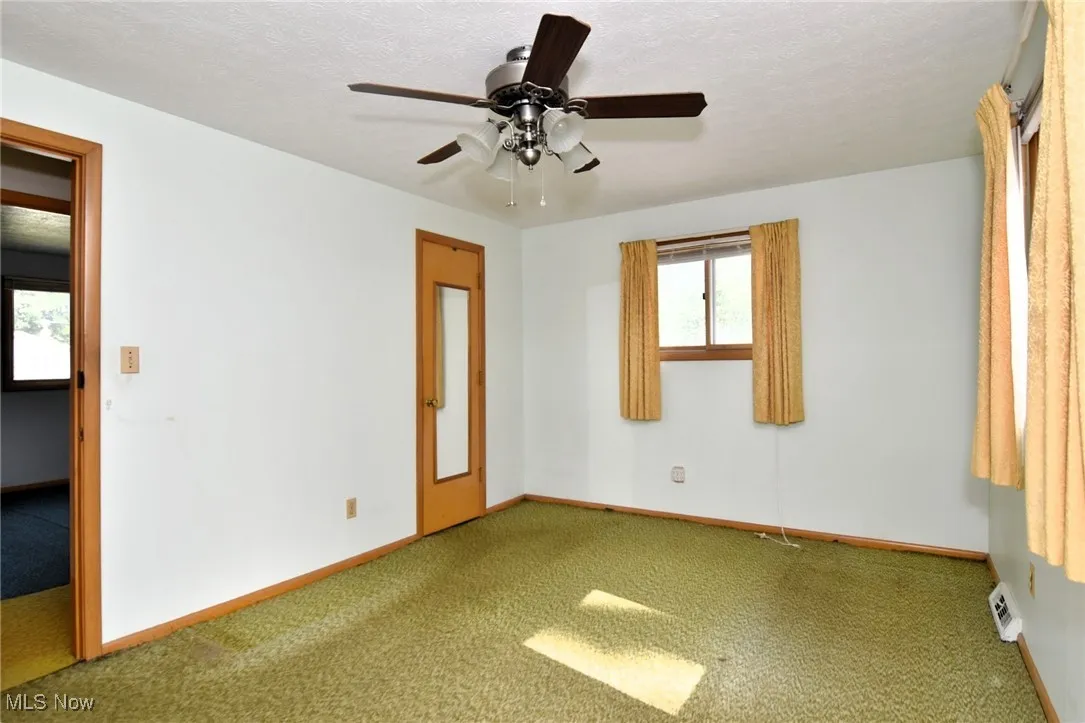 Spare room featuring carpet flooring, baseboards, ceiling fan, and a textured ceiling