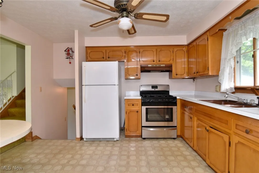 Kitchen featuring freestanding refrigerator, stainless steel range with gas stovetop, brown cabinetry, and light countertops