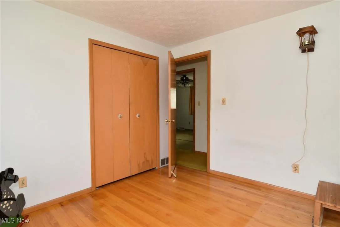 Unfurnished bedroom featuring light wood finished floors, baseboards, a textured ceiling, and a closet