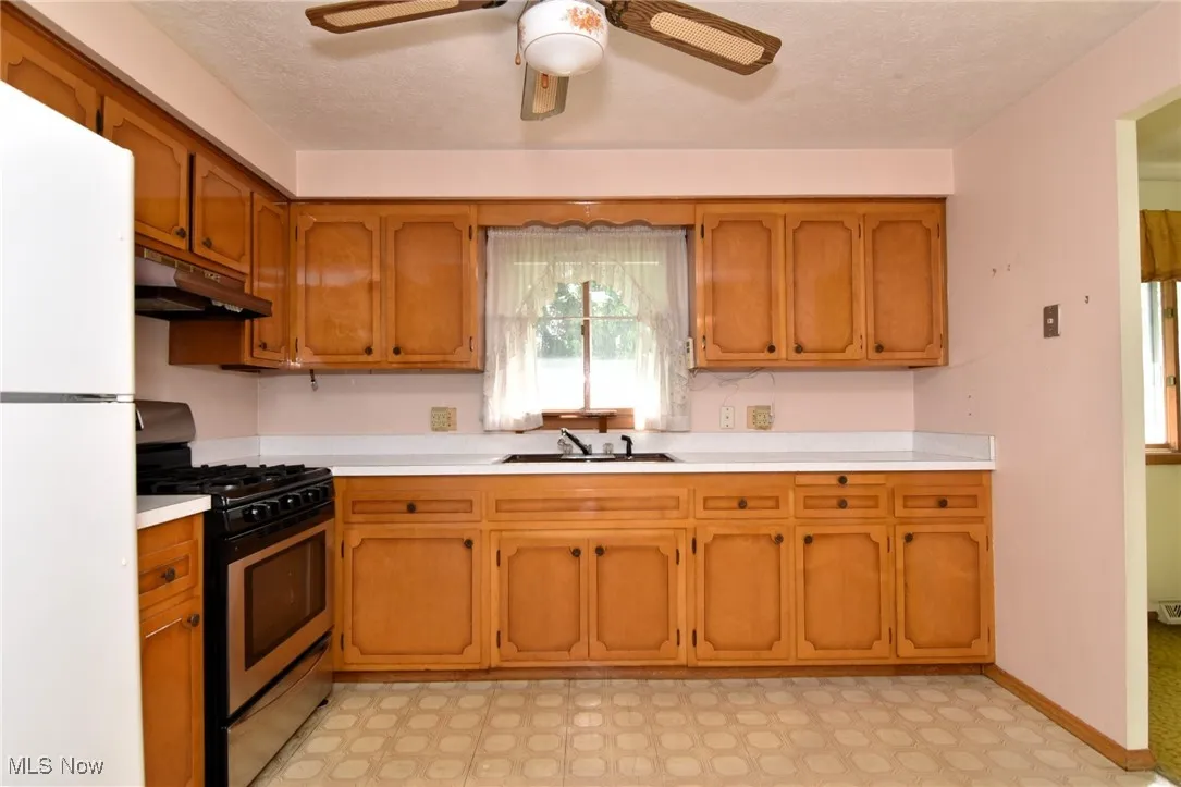Kitchen with gas stove, under cabinet range hood, freestanding refrigerator, a sink, and light countertops