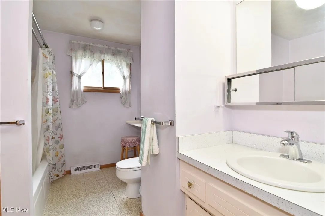 Bathroom featuring toilet, vanity, shower / tub combo with curtain, tile patterned floors, and baseboards