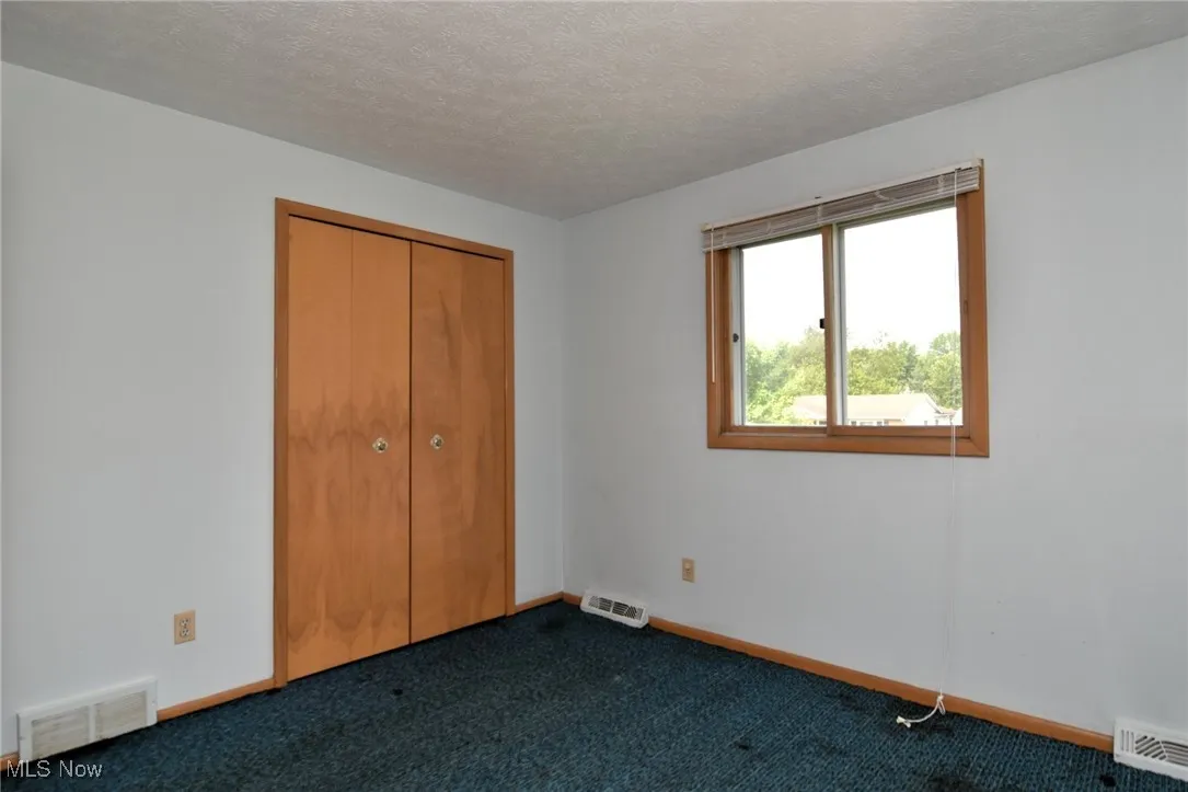 Unfurnished bedroom with dark carpet, a closet, a textured ceiling, and baseboards