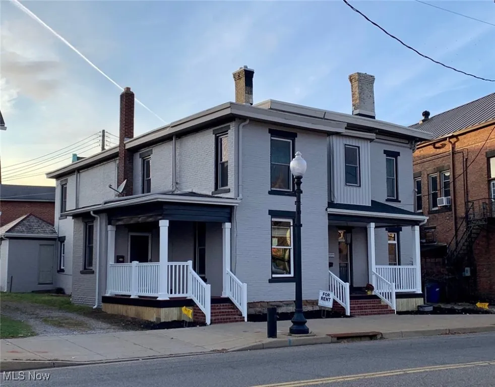 View of front of home featuring covered porch, brick siding, and a chimney