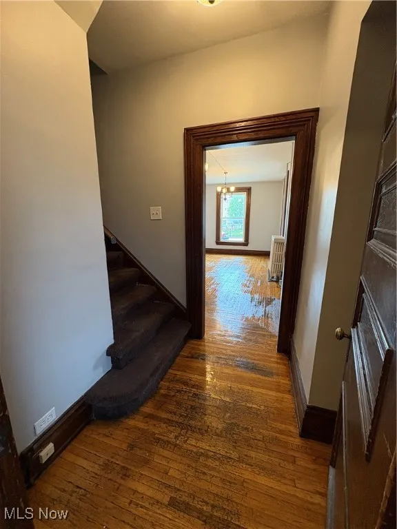 Corridor featuring hardwood / wood-style flooring, stairs, baseboards, a chandelier, and radiator