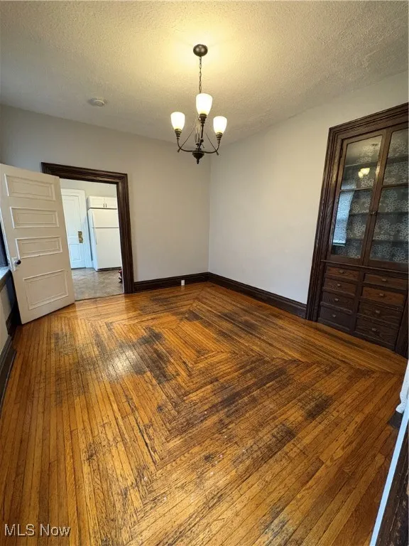 Unfurnished room featuring a chandelier, baseboards, and a textured ceiling
