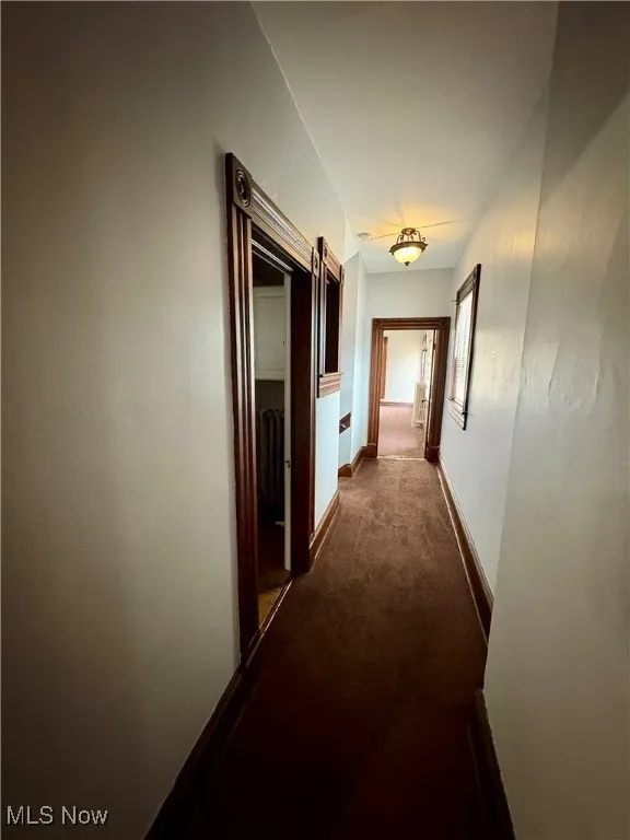 Hall with dark carpet, baseboards, and radiator heating unit