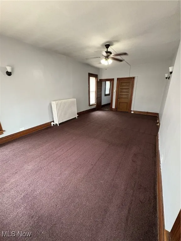 Spare room with radiator heating unit, a ceiling fan, dark carpet, and baseboards