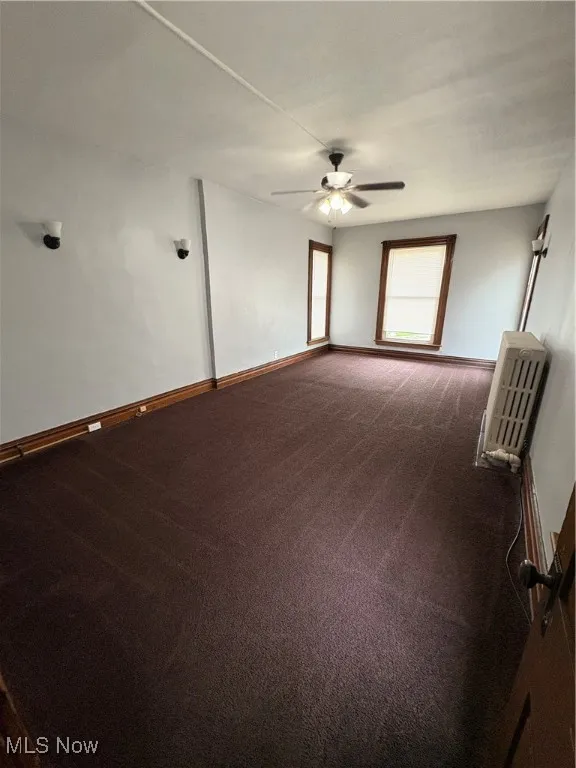 Unfurnished room featuring dark carpet, ceiling fan, and baseboards