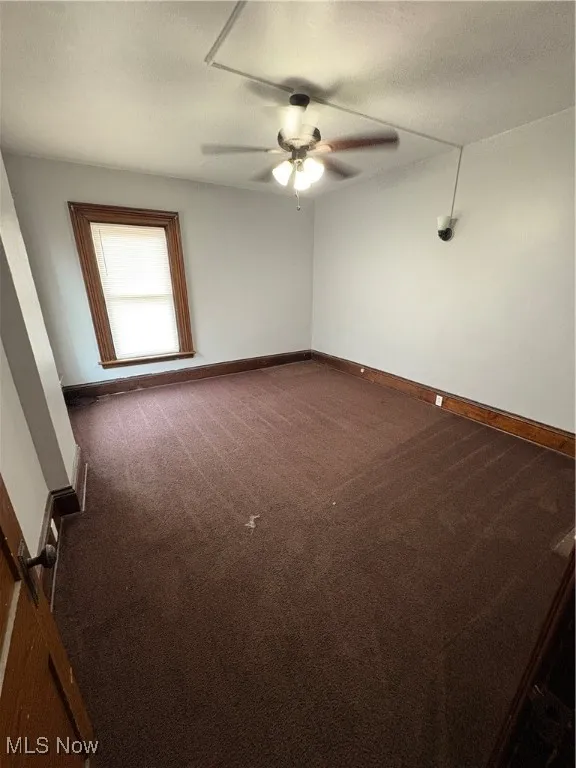 Unfurnished room with dark colored carpet, a ceiling fan, and baseboards