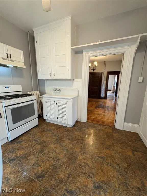 Kitchen with range, range hood, a chandelier, white cabinets, and light countertops
