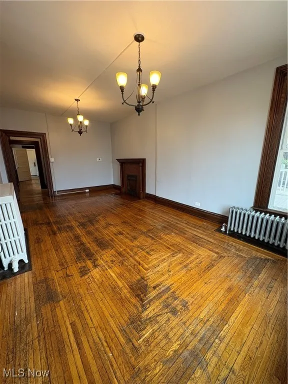 Unfurnished living room featuring radiator, a chandelier, and baseboards
