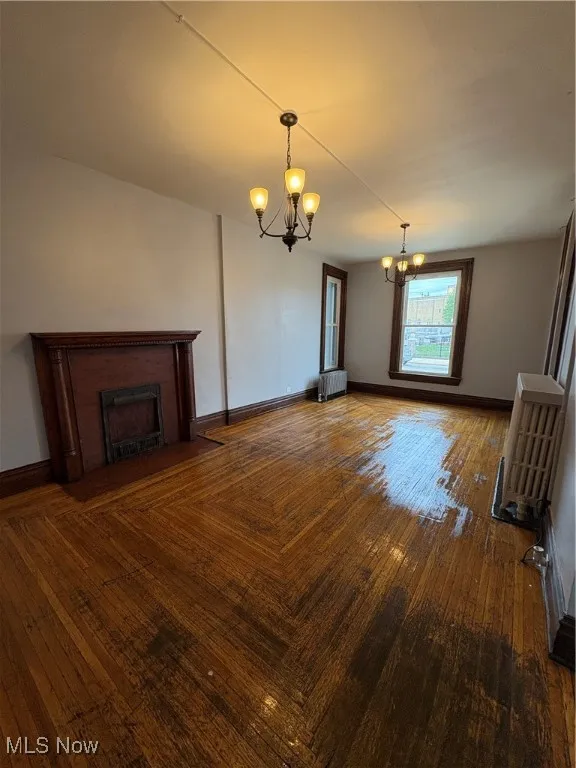 Unfurnished living room featuring a chandelier, a fireplace with flush hearth, and baseboards