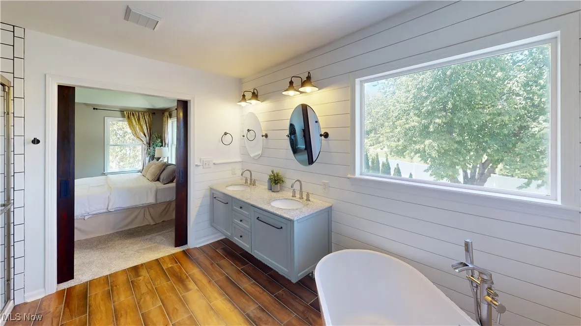 Ensuite bathroom with double vanity, a soaking tub, wood finished floors, wooden walls, and an enclosed shower