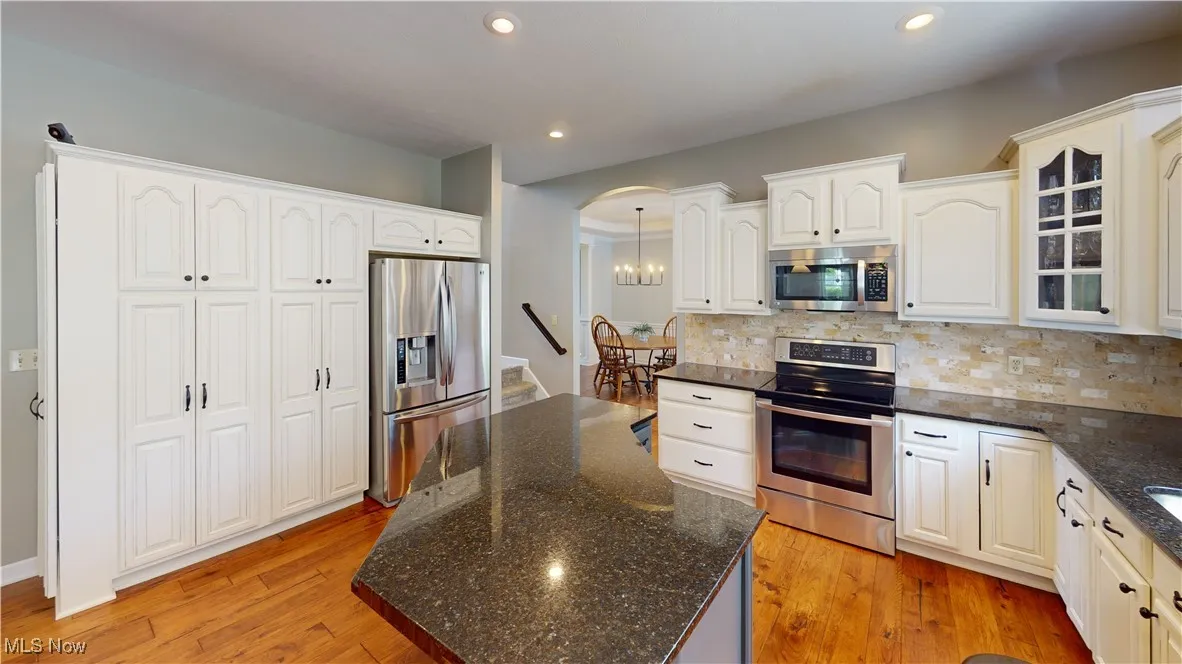 Kitchen with appliances with stainless steel finishes, backsplash, glass insert cabinets, recessed lighting, and dark stone counters