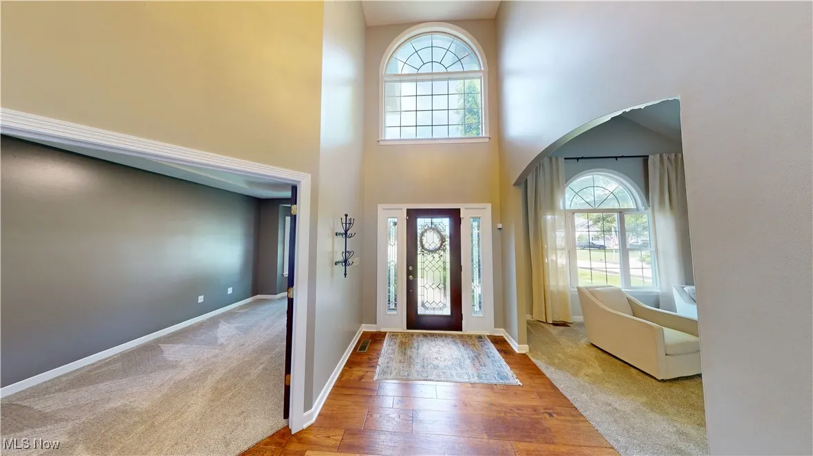 Carpeted entrance foyer with arched walkways, a high ceiling, wood-type flooring, and baseboards