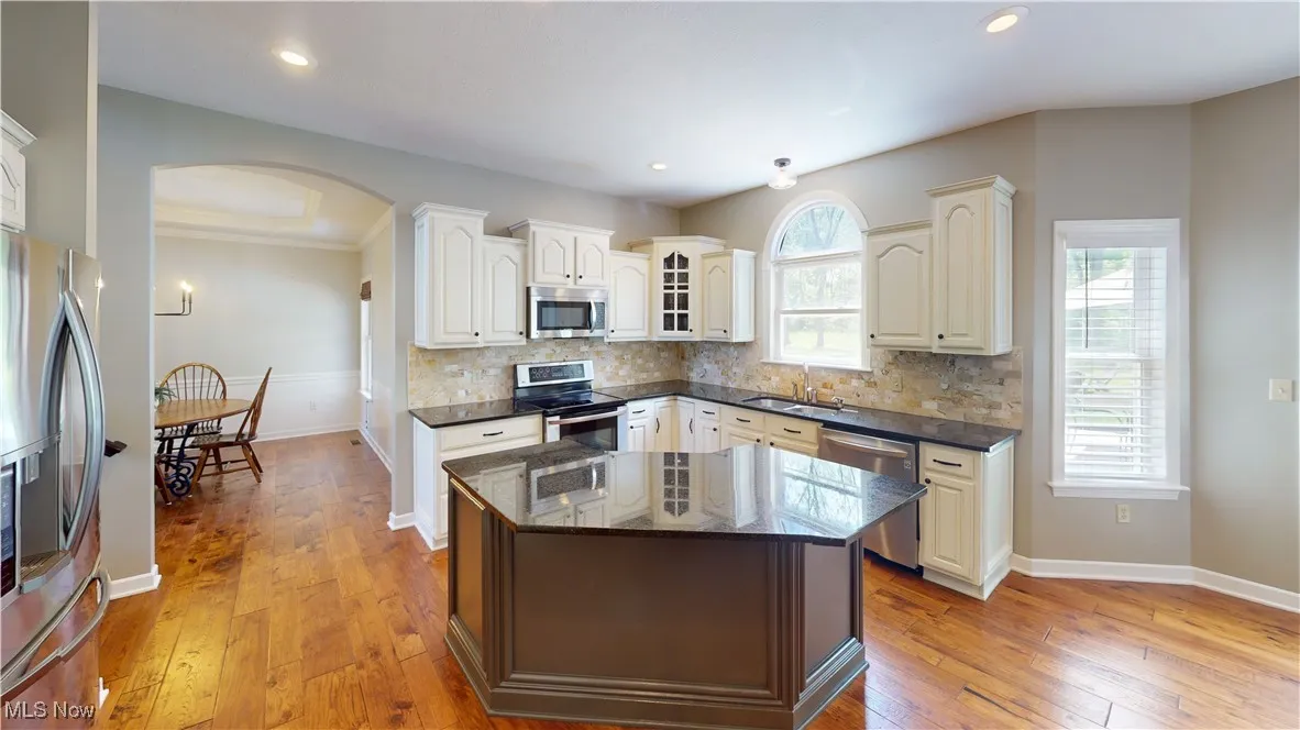 Kitchen with stainless steel appliances, arched walkways, a sink, light wood-style floors, and decorative backsplash