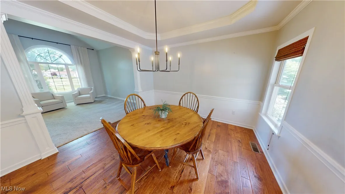Dining room featuring a chandelier, wood-type flooring, baseboards, crown molding, and a tray ceiling
