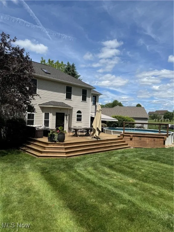 Rear view of house with an outdoor pool, a deck, a yard, and a shingled roof