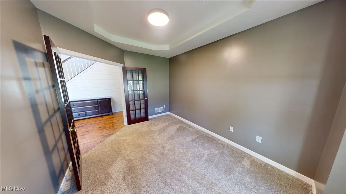Carpeted empty room featuring french doors, baseboards, and a raised ceiling