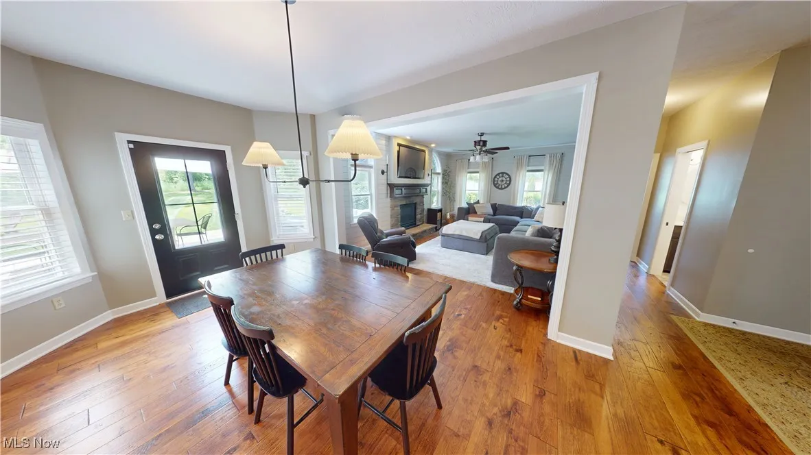 Dining area featuring a fireplace with raised hearth, hardwood / wood-style floors, a ceiling fan, and baseboards