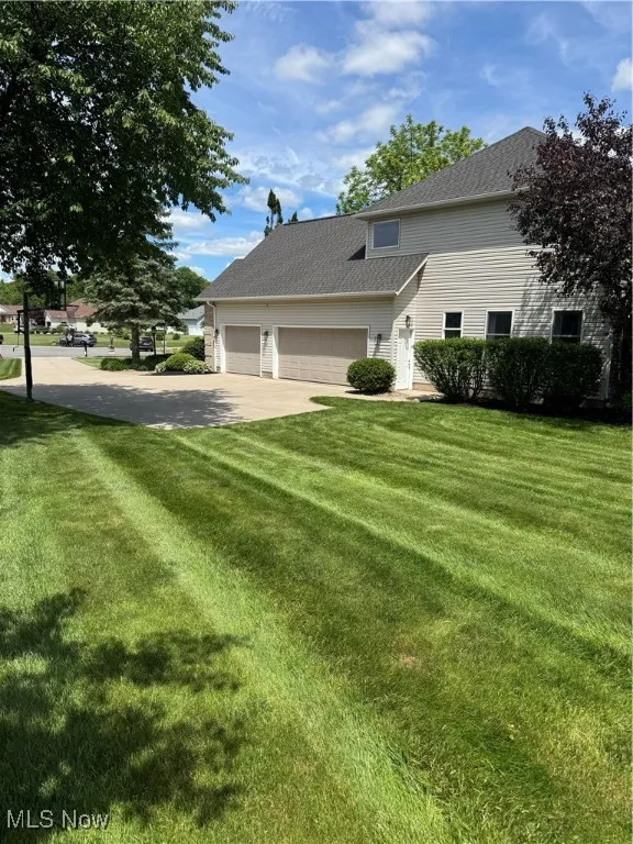 View of front of property with a front yard, a garage, concrete driveway, and a shingled roof