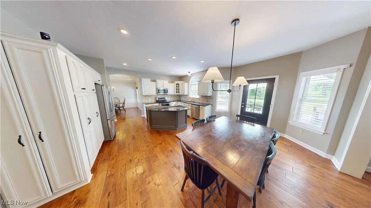 Dining space with arched walkways, light wood finished floors, recessed lighting, and baseboards