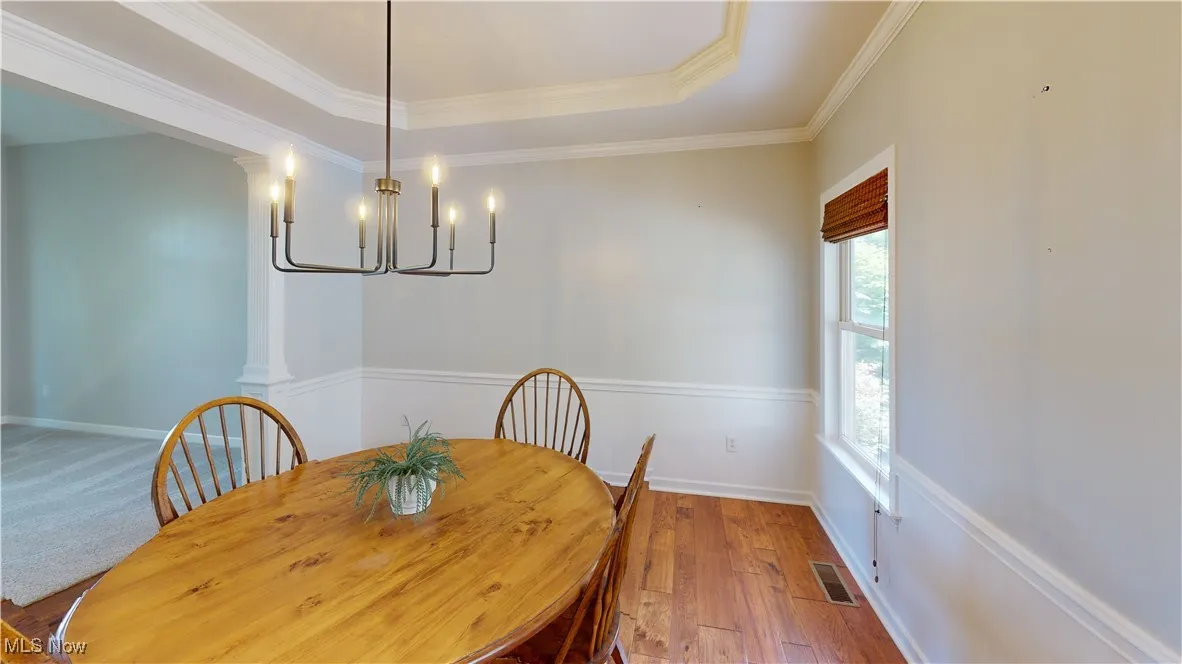 Dining area with a chandelier, crown molding, hardwood / wood-style flooring, a raised ceiling, and ornate columns