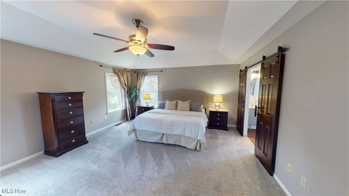 Bedroom with a barn door, light colored carpet, baseboards, and a ceiling fan