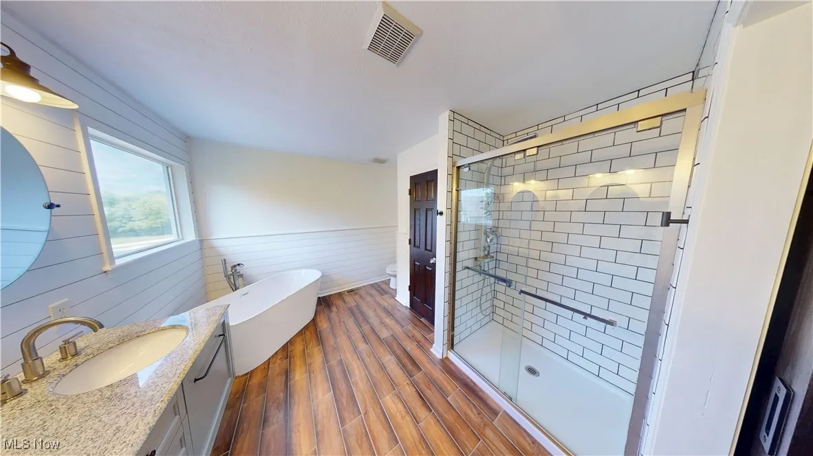 Bathroom with vanity, toilet, a stall shower, a freestanding tub, and wood walls