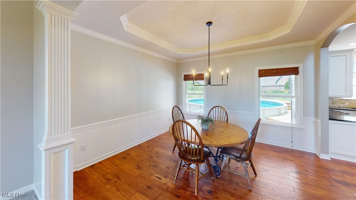 Dining room with a tray ceiling, hardwood / wood-style flooring, arched walkways, a chandelier, and crown molding