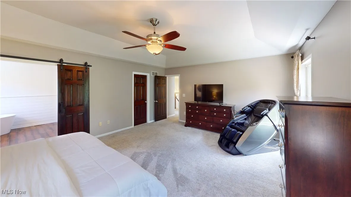 Bedroom with a barn door, carpet, ceiling fan, and baseboards