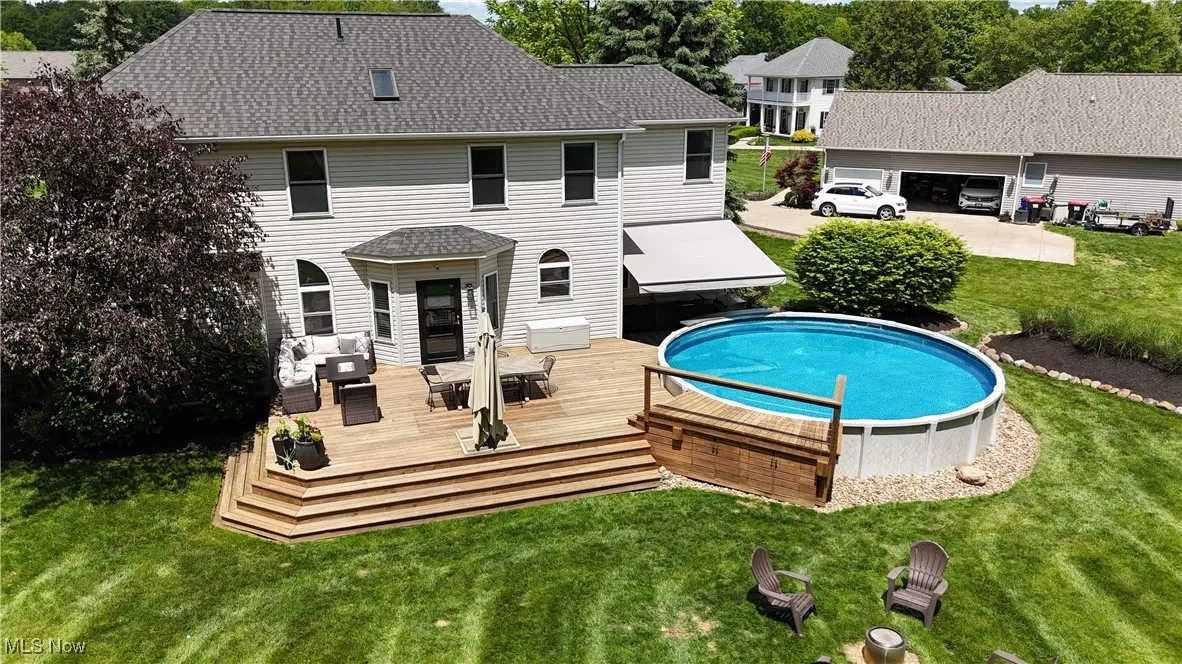 Rear view of house featuring a wooden deck, a lawn, an outdoor living space, an outdoor pool, and roof with shingles