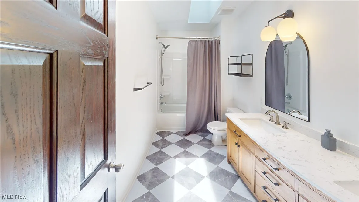 Bathroom featuring double vanity, a skylight, toilet, tile patterned floors, and shower / bathtub combination with curtain