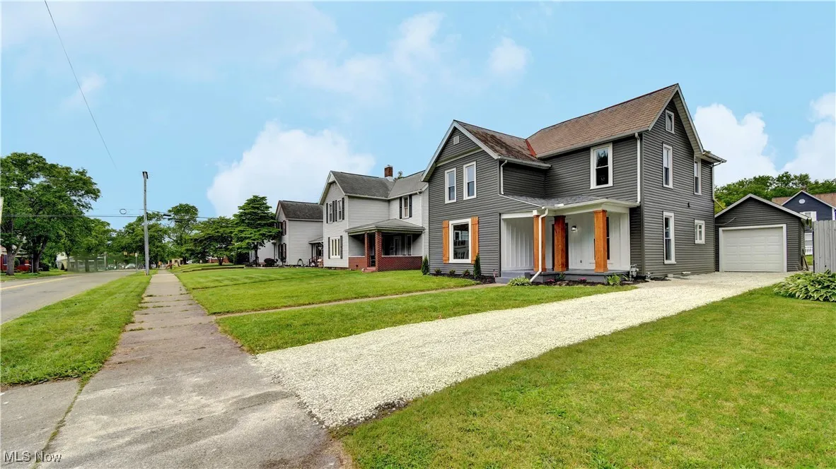 View of front of property with an outbuilding, driveway, a front yard, a detached garage, and a shingled roof