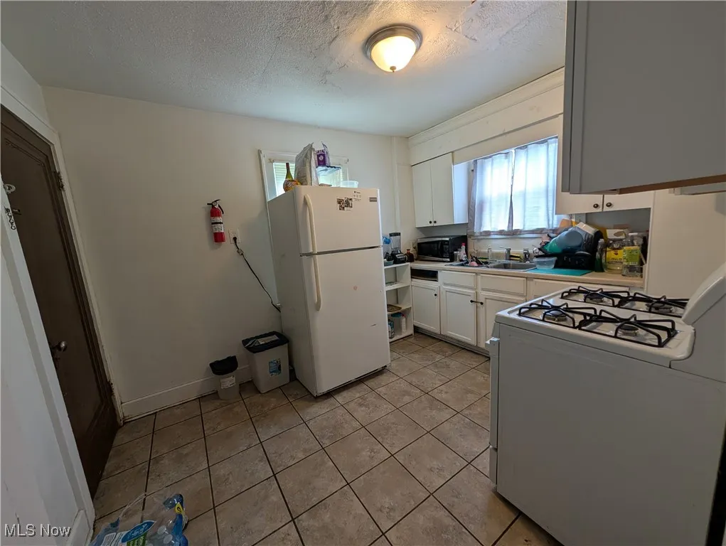 Kitchen with white appliances, plenty of natural light, white cabinets, a textured ceiling, and light tile patterned flooring
