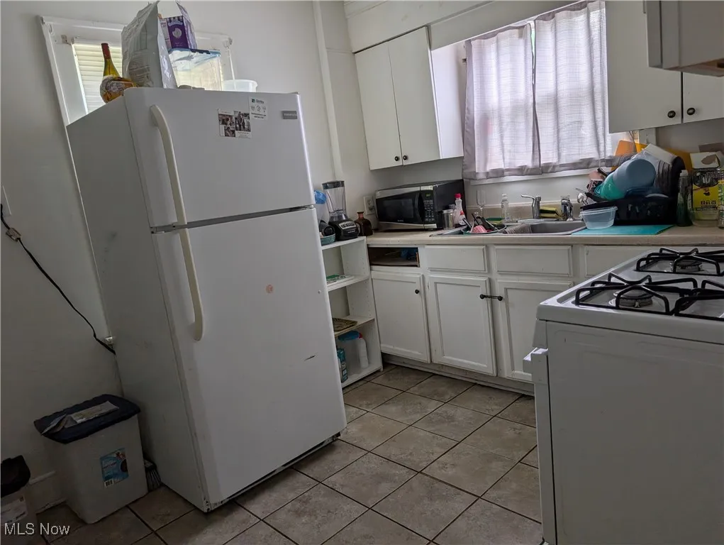 Kitchen with white appliances, a sink, light tile patterned floors, and white cabinetry