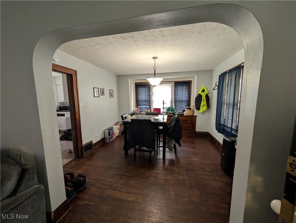 Dining room with arched walkways, hardwood / wood-style flooring, baseboards, and a textured ceiling