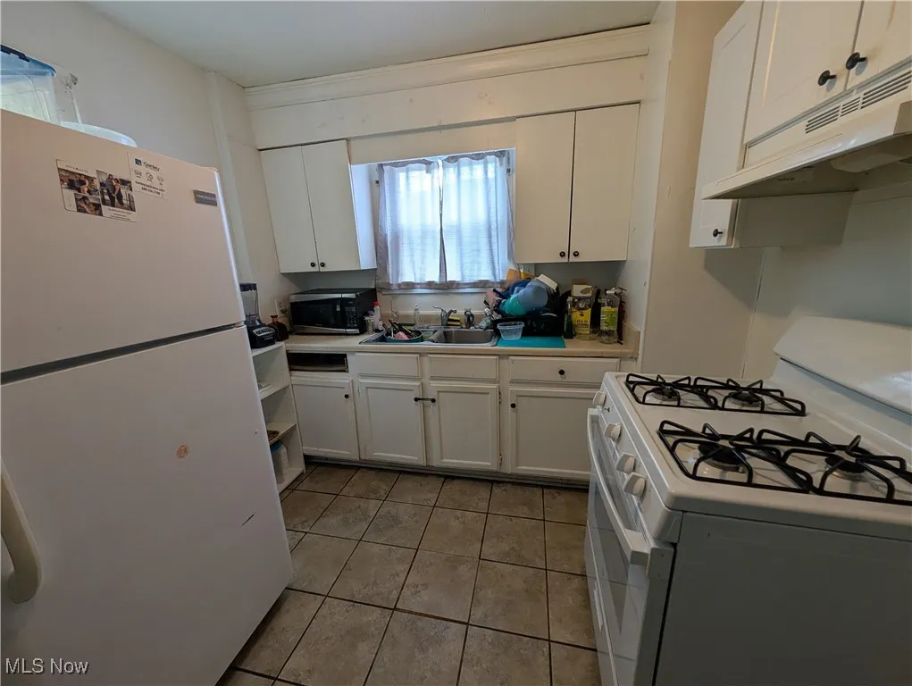Kitchen with white appliances, under cabinet range hood, white cabinetry, light tile patterned floors, and light countertops