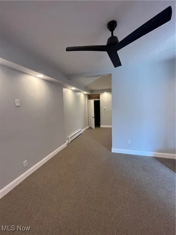 Unfurnished room featuring baseboard heating, ceiling fan, dark colored carpet, and baseboards