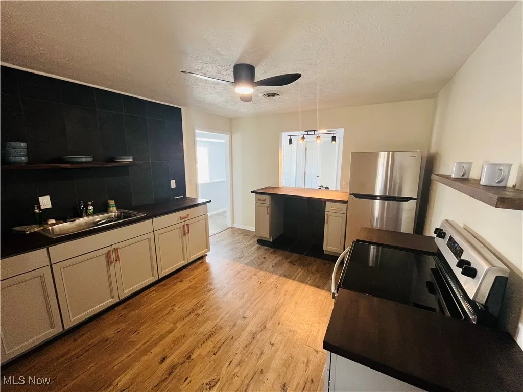 Kitchen with freestanding refrigerator, a sink, a textured ceiling, ceiling fan, and light wood finished floors