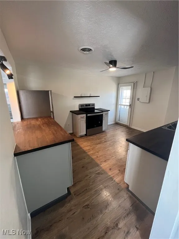 Kitchen with electric range, dark wood finished floors, ceiling fan, a textured ceiling, and wood counters