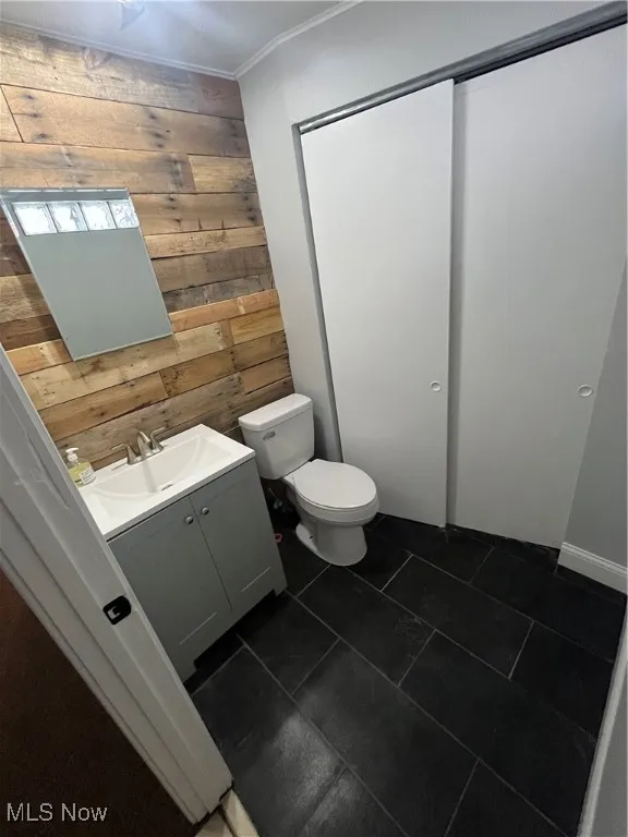 Half bathroom featuring wooden walls, vanity, toilet, tile patterned flooring, and ornamental molding