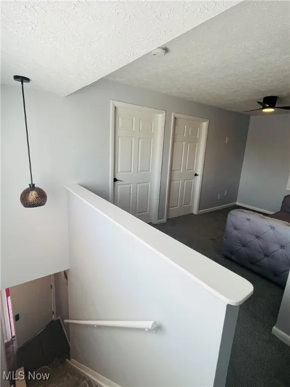 Stairway featuring a textured ceiling, baseboards, ceiling fan, and carpet flooring
