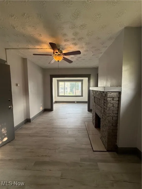 Unfurnished living room with light wood-type flooring, a textured ceiling, baseboards, a fireplace, and ceiling fan