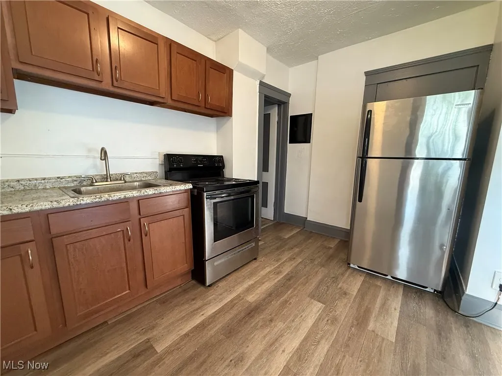 Kitchen featuring stainless steel appliances, a sink, light wood-style floors, a textured ceiling, and brown cabinets