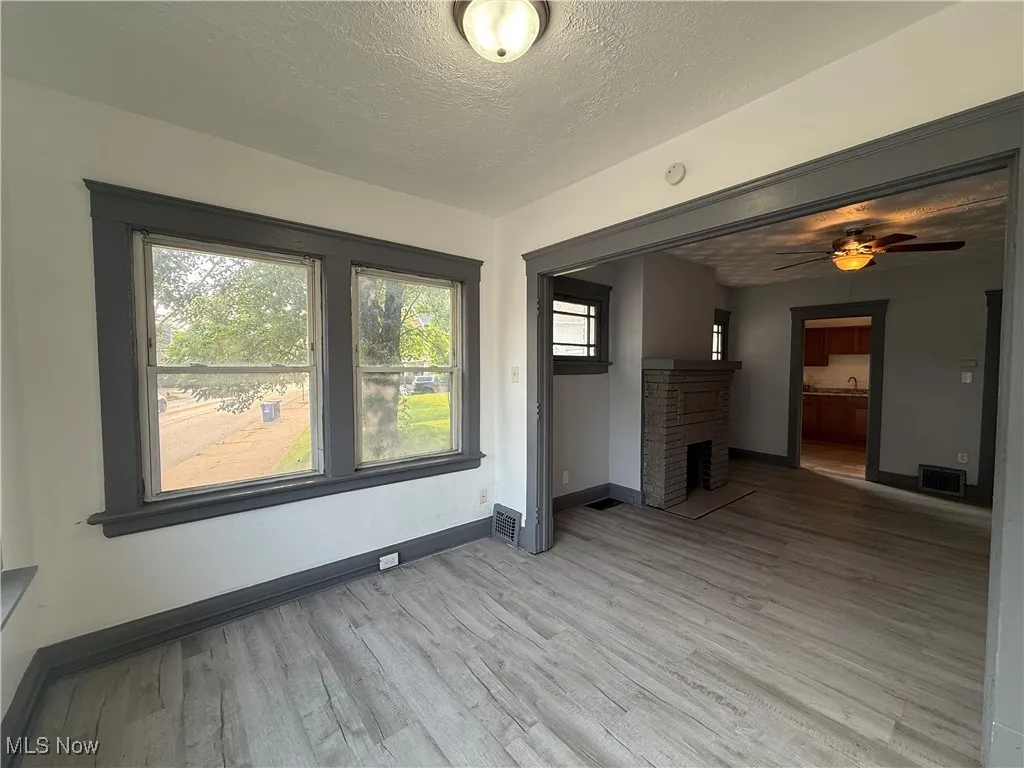 Unfurnished living room with light wood-type flooring, a textured ceiling, baseboards, a ceiling fan, and a fireplace