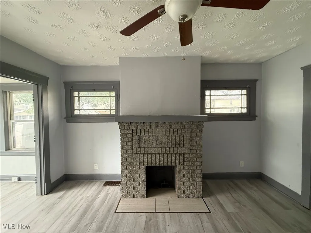 Unfurnished living room featuring wood finished floors, baseboards, ceiling fan, healthy amount of natural light, and a textured ceiling