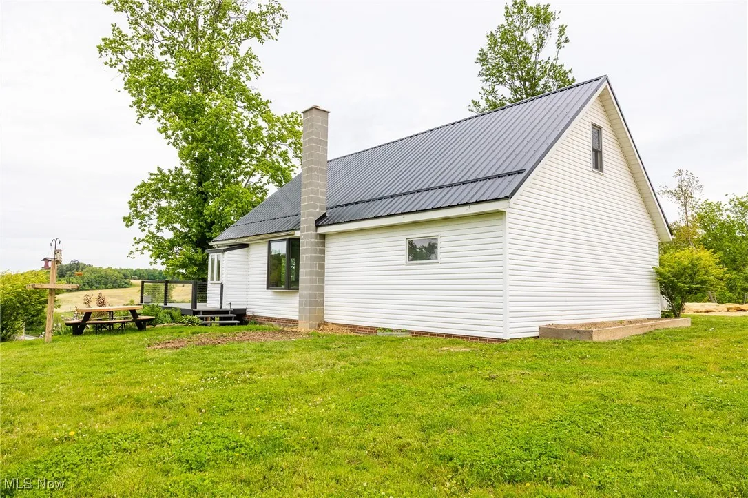 Rear view of property featuring a yard, a chimney, a deck, and metal roof