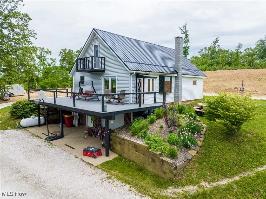 View of front of home with a balcony, a chimney, a wooden deck, metal roof, and a patio